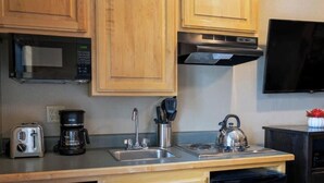 Una cocina con armarios de madera, microondas, tostadora, cafetera, hervidor de agua, lavavajillas y televisor montado sobre la encimera.