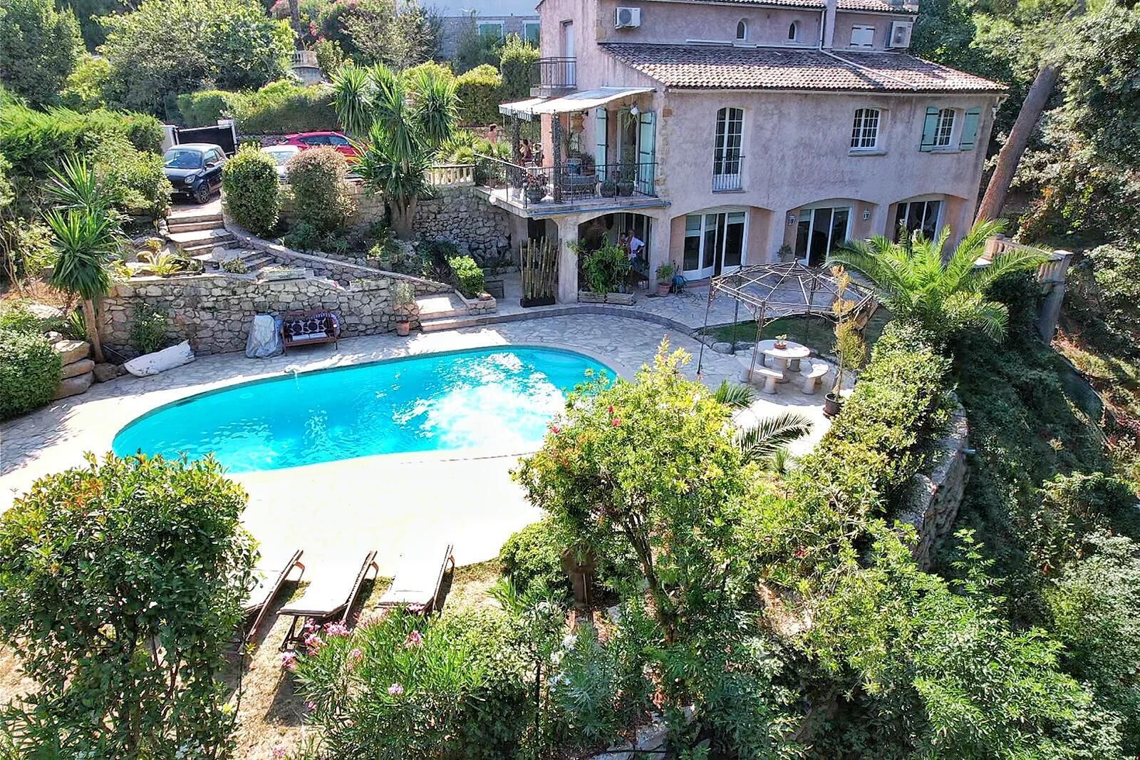 Una gran piscina rodeada de exuberante vegetación, un muro de piedra y un edificio de varios pisos con balcones.