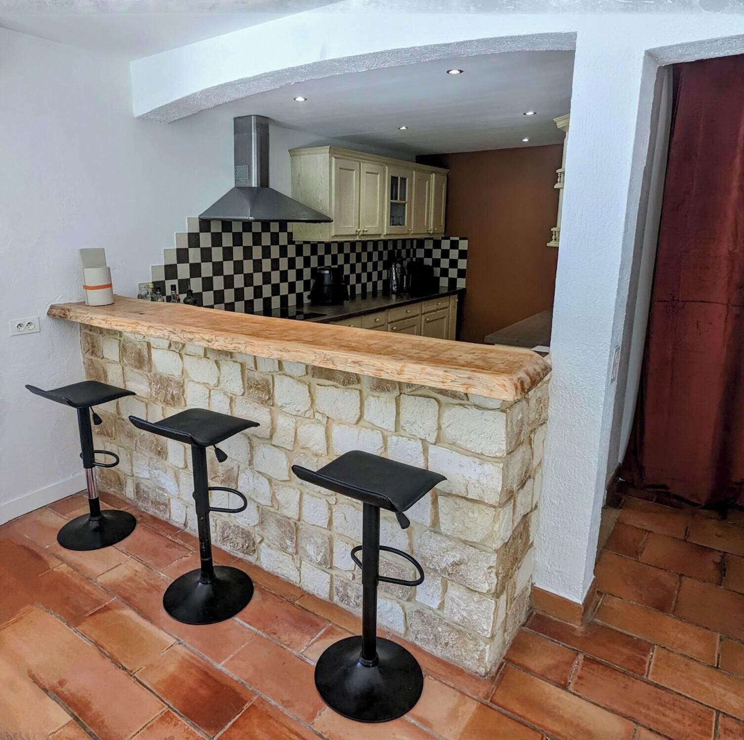 Une cuisine avec un dosseret à carreaux, un îlot central en pierre avec des tabourets de bar et une cheminée.