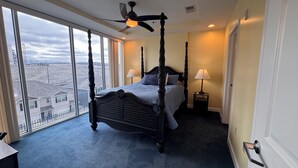 A four-poster bed with a ceiling fan, a nightstand with a lamp, and a view of a snowy landscape through large windows.