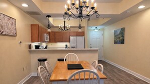 A dining area with a wooden table and white chairs, a chandelier, wooden cabinets, and a white door.