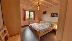 Ein Schlafzimmer einer Holzhütte mit Bett, einem Fenster mit Vorhängen, einem Wandbild und einer Deckenleuchte.