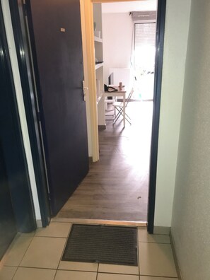 Un couloir mène à une pièce dotée d’une porte sombre, d’un sol carrelé et d’une petite table entourée de chaises.