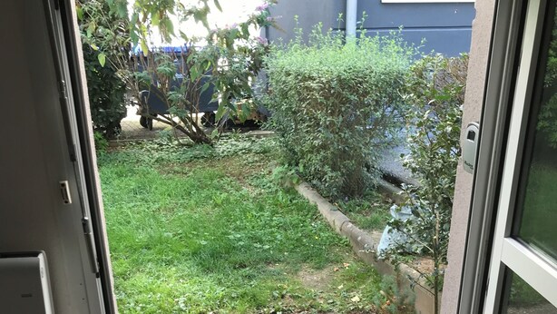 A doorway leading to a garden with a gravel path, a small tree, and a wheelbarrow. - Charming studio near downtown (Strasbourg)