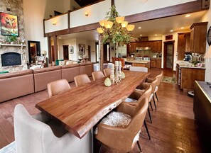 Un vaste espace de vie comprenant une grande table à manger en bois, des canapés en cuir et une cuisine située à l’arrière-plan.