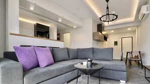 A modern living room with a grey sectional sofa, a glass coffee table, and a chandelier.