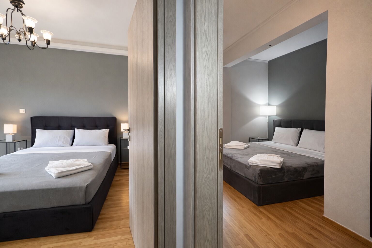 A hotel room with two beds, a wooden floor, and a chandelier.