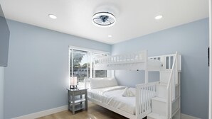 A bedroom with a bunk bed, a bedside table, a lamp, and a window with blinds. - Modern 4BR Home, Sleeps 9, Near Silicon Valley (San Jose)