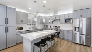 A modern kitchen with grey cabinets, stainless steel appliances, a central island with bar stools, and pendant lighting. - Modern 4BR Home, Sleeps 9, Near Silicon Valley (San Jose)