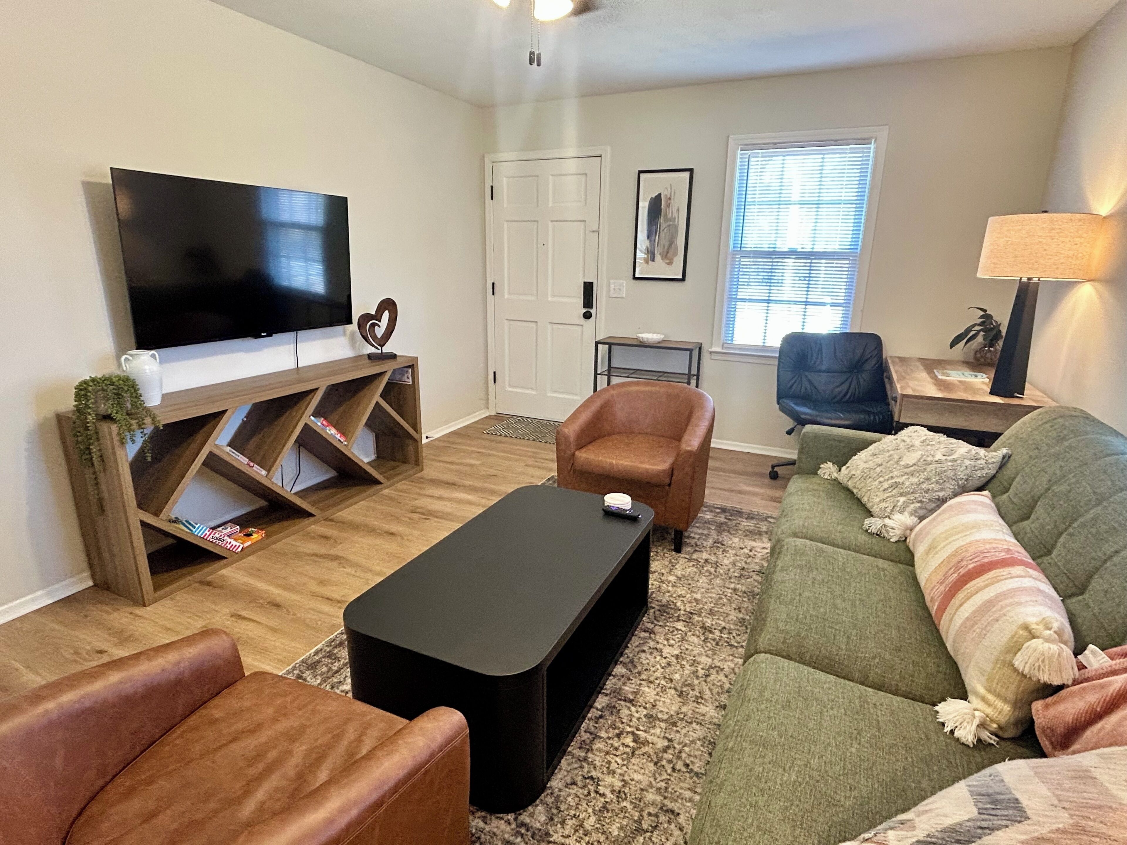 A living room with a flat-screen TV, a brown leather armchair, a green sofa, and a black coffee table.