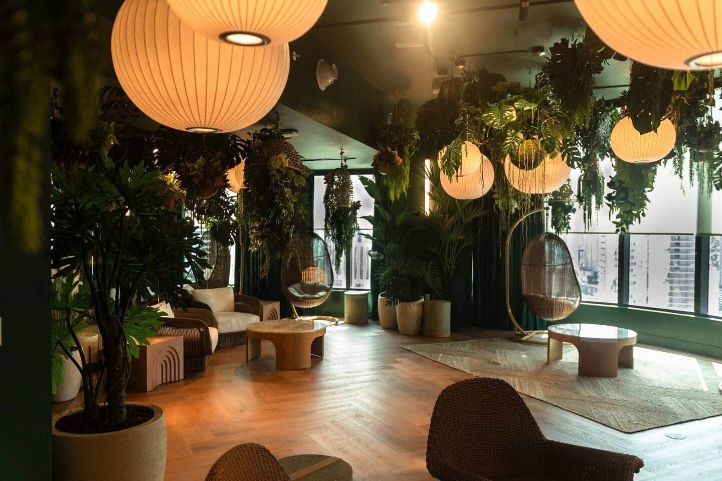 Ein Lounge-Bereich mit runden Tischen, bequemen Sitzgelegenheiten, hängenden Pflanzen und großen Fenstern.