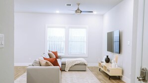 A modern living room with a sofa, ottoman, and a flat-screen TV mounted on the wall. - Down-Town/ Alamo dome/tower of americas/ hemisphere park (San Antonio)