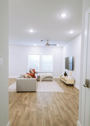 Un salon moderne avec un canapé, un pouf et un téléviseur à écran plat fixé au mur.