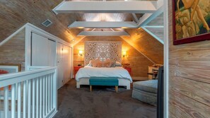 A bedroom with a sloped ceiling, a bed, a nightstand, a chair, and a wall-mounted lamp. - Pineapple Conch House (Key West)
