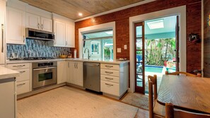 A modern kitchen with white cabinetry, stainless steel appliances, and a view of a pool through a glass door. - Pineapple Conch House (Key West)