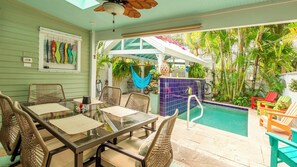 A poolside area with a glass table, wicker chairs, a hammock, and a blue tiled wall. - Pineapple Conch House (Key West)