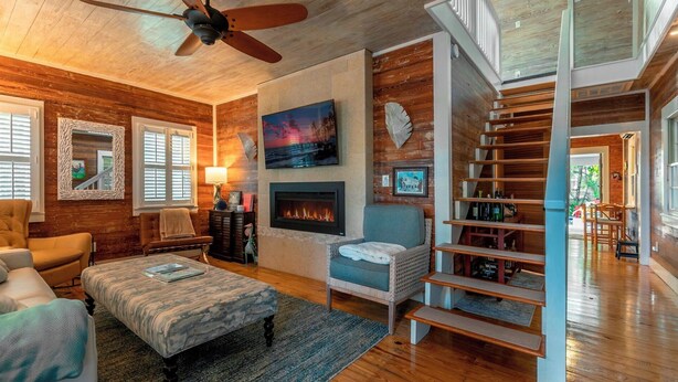 Una sala de estar acogedora con chimenea, escalera y ventilador de techo.