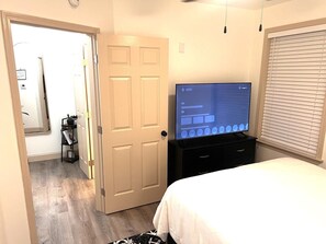 Une chambre d’hôtel avec un lit, un téléviseur posé sur un meuble, une porte et une fenêtre avec des stores.