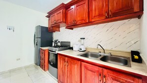 Een keuken met houten kastjes, een koelkast, fornuis, spoelbak en een blender.