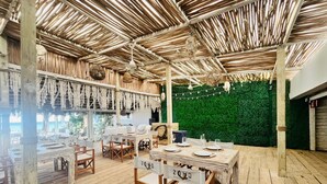 Een buiten eethoek met houten tafels en stoelen, een groene wand en een rieten dak.