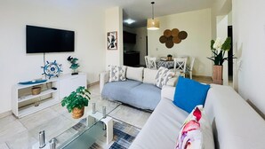 Een moderne woonkamer met een bank, televisie en een eethoek met een tafel en stoelen.