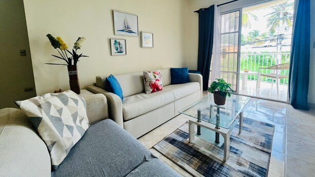 Een woonkamer met een bank, een bijzettafeltje en uitzicht op een balkon.