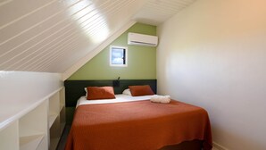 Ein Schlafzimmer mit schrägen Wänden, einer Klimaanlage, einem Fenster und einem Bett mit Decke.