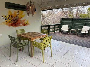 An outdoor patio with a wooden table and chairs, a hanging light fixture, and a mural of a bird on the wall. - Sloke - The green flamingo (Sint Willibrordus)