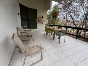 Un balcón con una mesa y sillas, una maceta colgante y un mural en la pared.