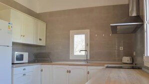 A kitchen with white cabinets, a microwave, a toaster, and a window with blinds.