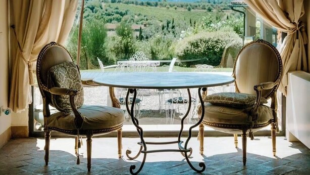 A room with a table and two chairs, a chandelier, and a view of a green landscape. - Villa La Serra-View and Charm in Tuscany (Toscana)