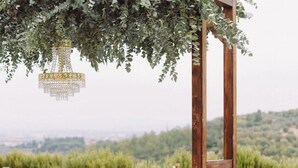 An outdoor dining setup with a white tablecloth, wicker chairs, and a wooden pergola with greenery. - Villa La Serra-View and Charm in Tuscany (Toscana)
