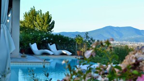 A pool with white lounge chairs, a view of a city and mountains in the background, and a garden with various plants. - Villa La Serra-View and Charm in Tuscany (Toscana)