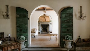 An arched doorway leading to a room with a fireplace, a dining table with chairs, and two large vases. - Villa La Serra-View and Charm in Tuscany (Toscana)
