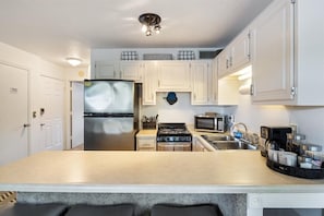 A modern kitchen with white cabinets, a stainless steel refrigerator, a stove, a microwave, and a sink. - Lakefront Bungalow Near Margaritaville (Osage Beach)