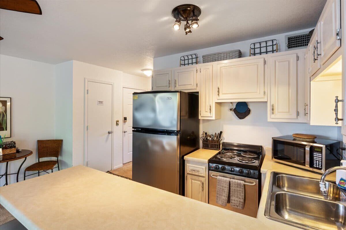 A compact kitchen with white cabinets, a stainless steel refrigerator, a microwave, a stove, and a sink.