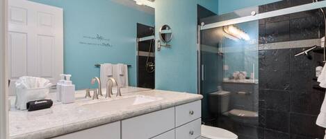 A bathroom with a blue wall, white vanity, and a glass-enclosed shower.