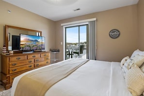 A hotel room with a large bed, a TV on a wooden dresser, a balcony with a view, and a 'believe' sign on the wall. - Lakefront Condo With Boat Slip (Osage Beach)