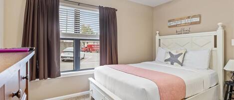 A bedroom with a bed, a window with curtains, a ceiling fan, and a wall with a sign.