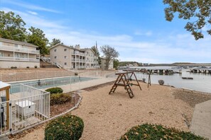 A waterfront property with a swimming pool, a swing set, and a building with multiple balconies. - Lakefront Condo With Boat Slip (Osage Beach)