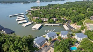 An aerial view of a lakeside resort with docked boats, a swimming pool, and multiple buildings surrounded by dense greenery. - Main Channel View, Playground, no Steps Enrty (Lake Ozark)