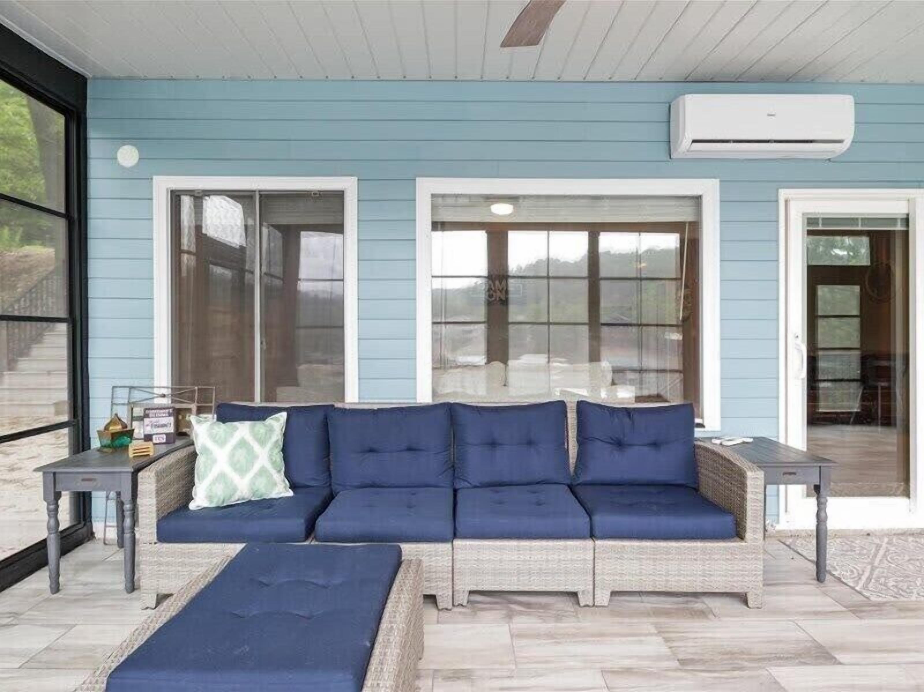 Un área de estar al aire libre con techo, una pared azul, ventanas amplias y un sofá de mimbre con cojines azules.