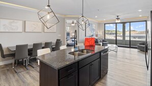 A modern kitchen with a central island, dining area with chairs, and large windows offering a view. - New Topsider Condo With Boat Slip (Osage Beach)