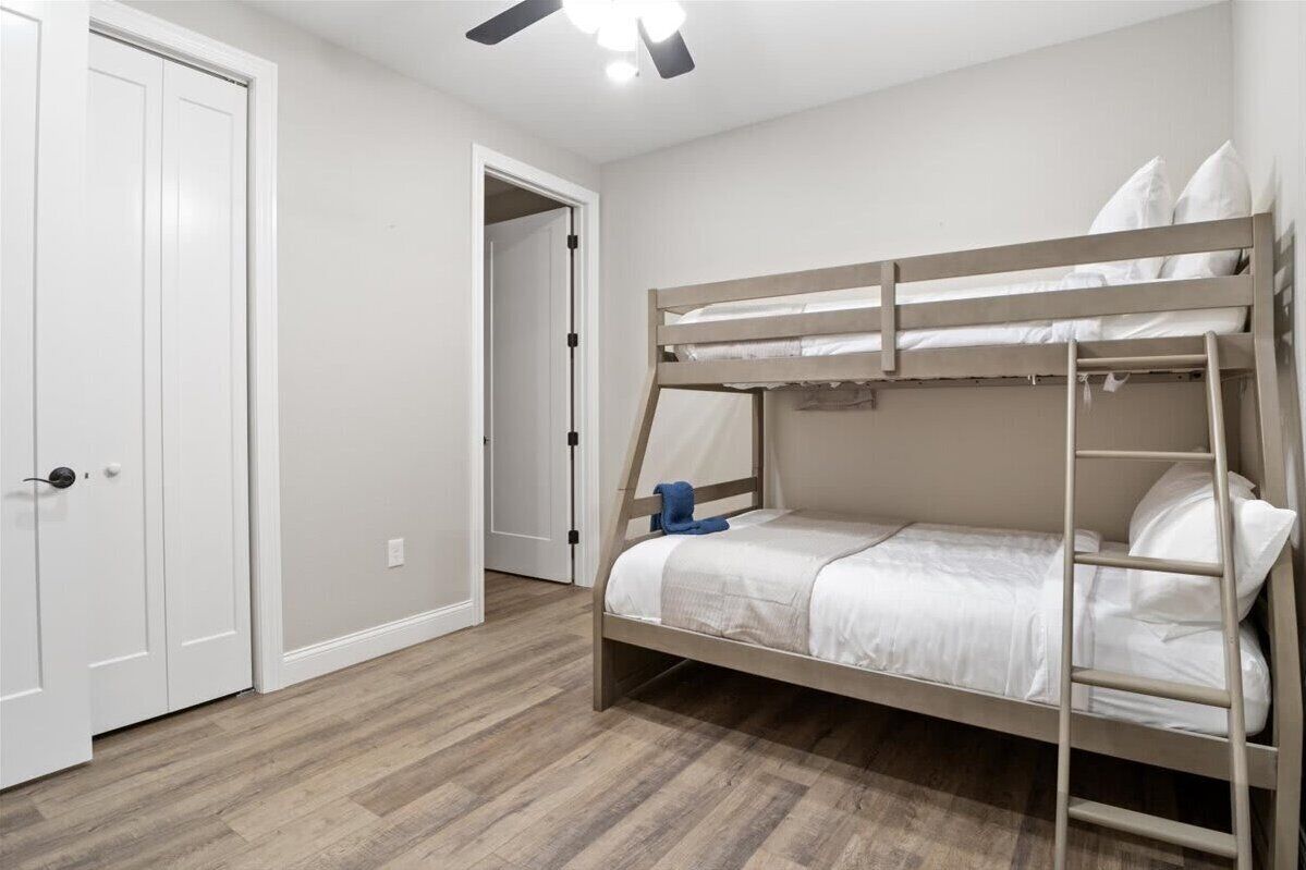 A bunk bed with a ladder, white bedding, and a wooden floor.