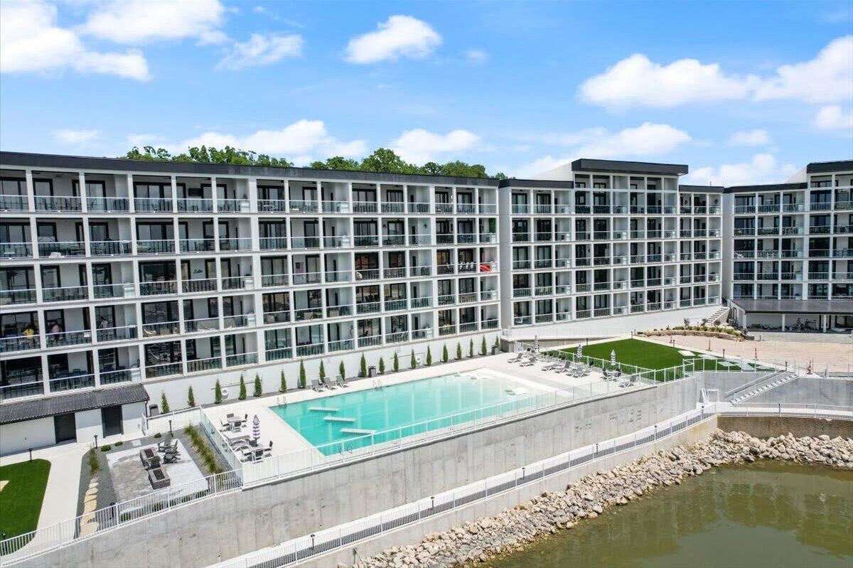 Un hotel moderno de varios pisos con piscina central, zona de estar exterior y jardines.
