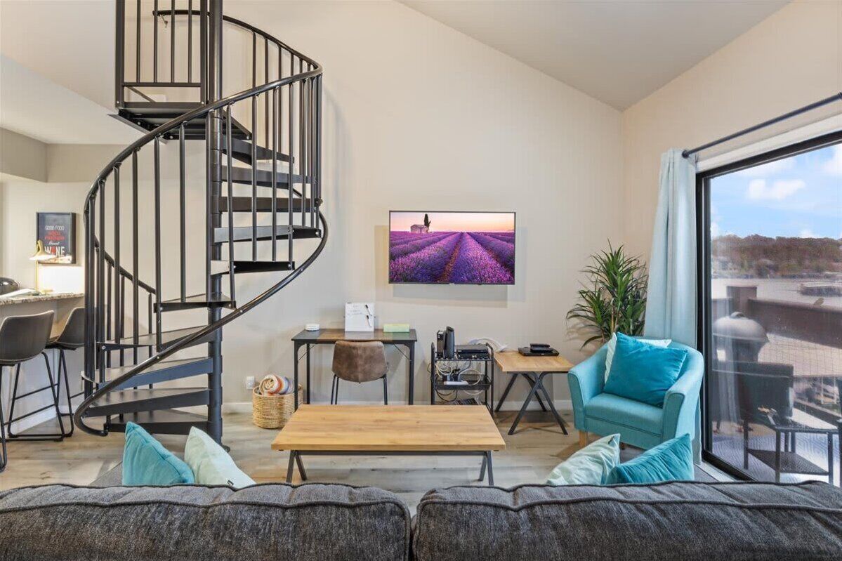 Una sala moderna con una escalera de caracol, un ventanal con vistas, un televisor de pantalla plana y un rincón de estar acogedor.