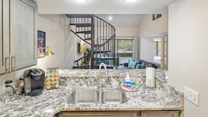 A kitchen with a marble countertop, double sink, coffee maker, and a coffee pod holder. - Lakefront Condo Indoor Pool, Sauna, & Pickle Ball! (Osage Beach)