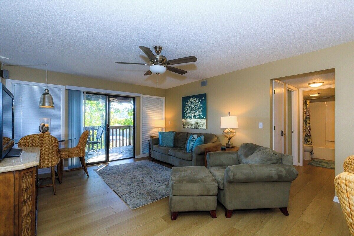 A spacious living room with a ceiling fan, a dining area with a table and chairs, and a large window with blinds.