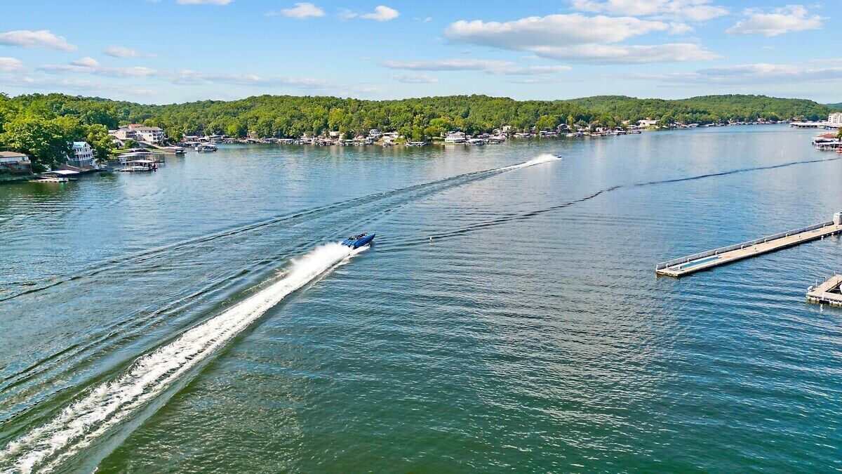 Ein Boot saust über den See, im Hintergrund ein Steg und Gebäude.