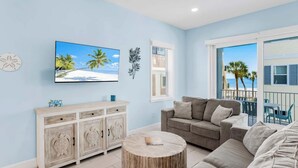 A living room with a sofa, a coffee table, a TV, and a view of the beach. - 4BR Beachfront Balcony Condo | Partial Ocean View (Indian Shores)